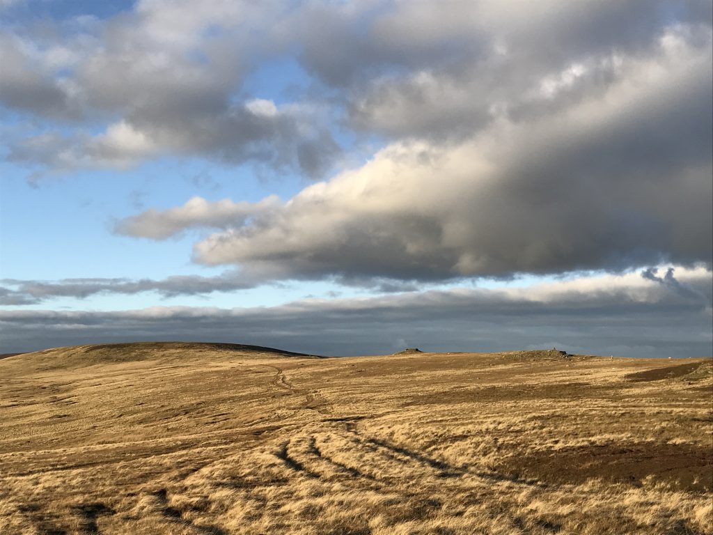 The sun shines on moorland with moody clouds above