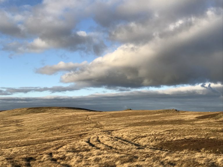 The sun shines on moorland with moody clouds above